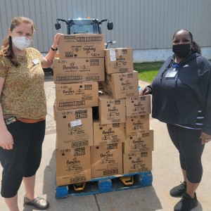 two people stand next to a pallet of diapers outside the River Food Pantry