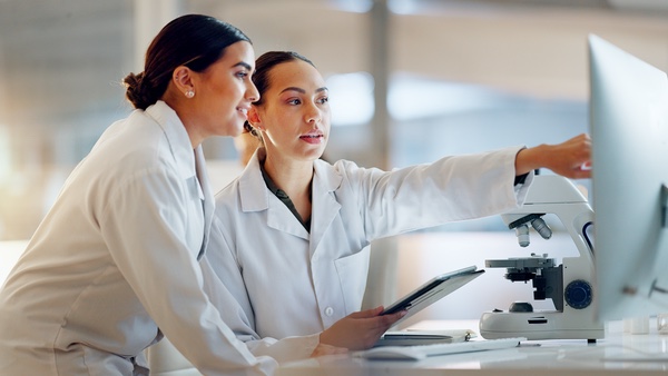 Two people in white coats look at a computer screen together